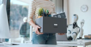 Fired office worker leaving her workplace and humanoid robot staring at her: the impact of AI on employment. Image credit: Shutterstock